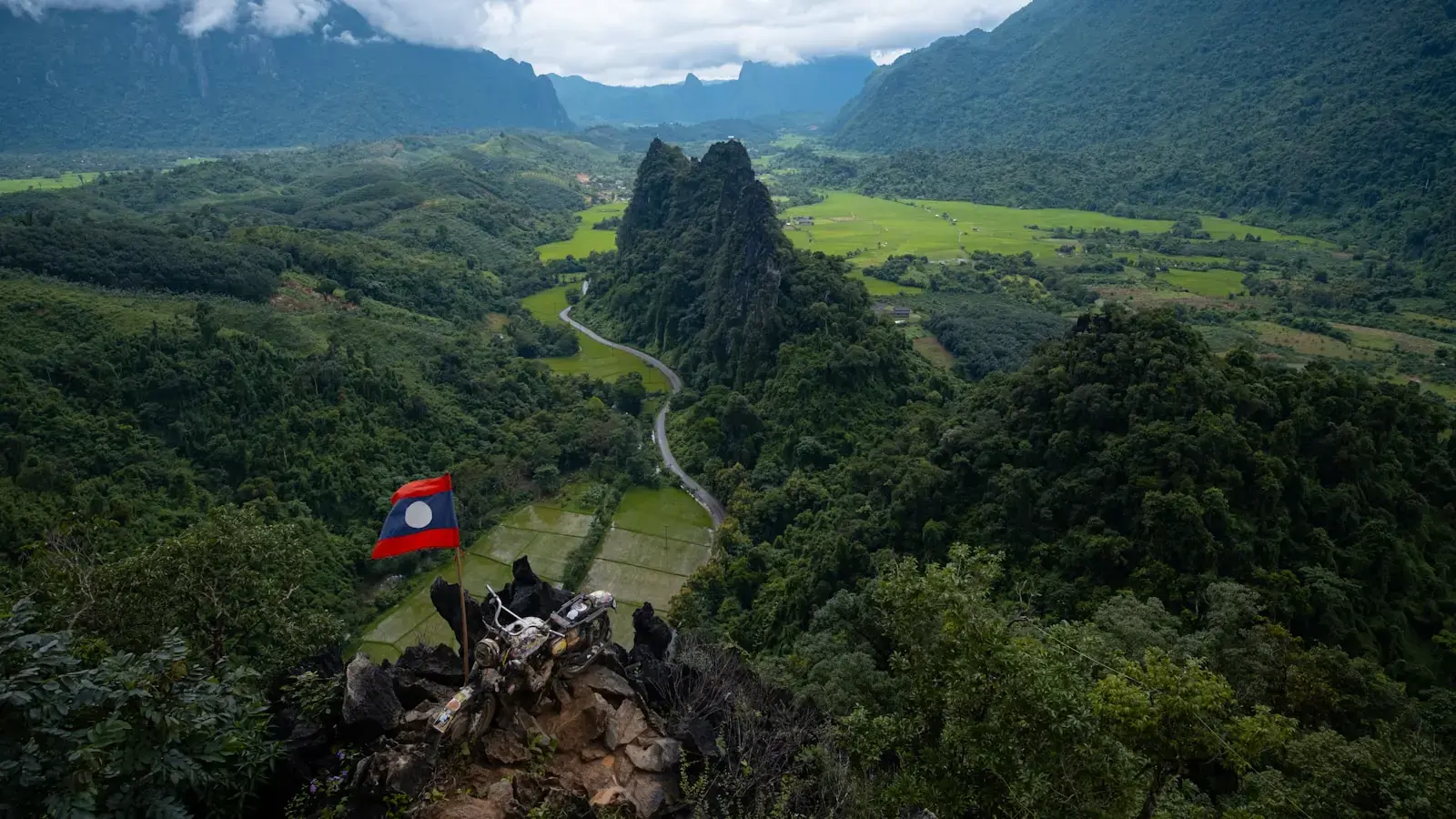 Lush green valley with a winding road and flag