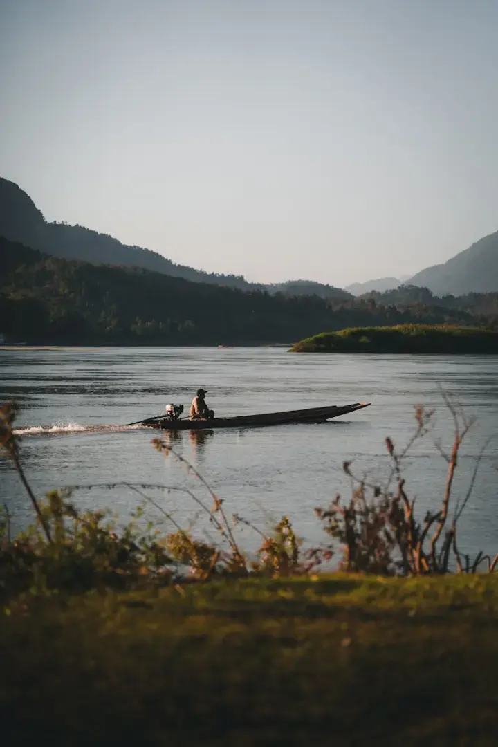 Photo by Kevin Charit Man on a long boat traveling on a wide river.