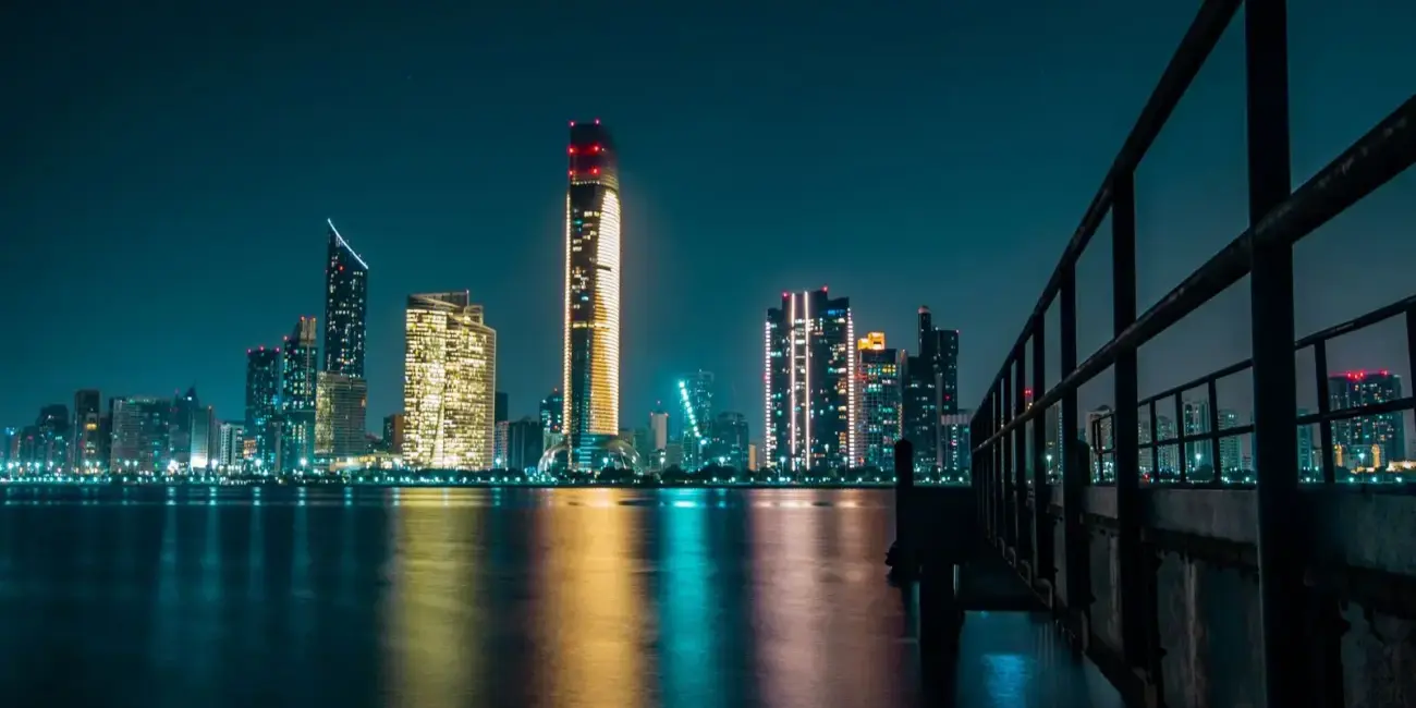 Stunning Abu Dhabi skyline at night with city lights reflecting off the calm waterfront.