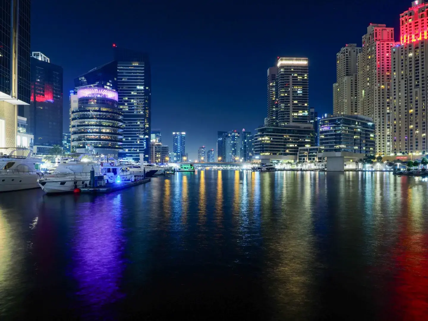 The illuminated skyline of Dubai Marina reflects on peaceful waters under a clear night sky.