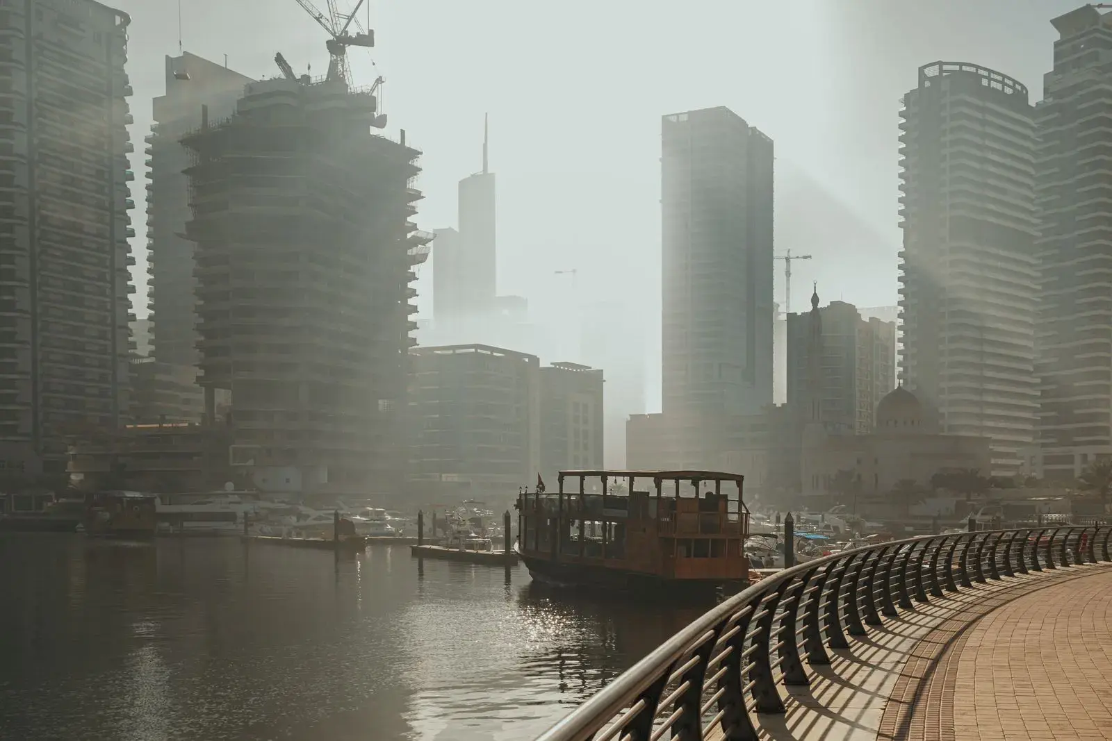 Serene fog envelops Dubai Marina's skyscrapers with a classic dhow on tranquil waters.