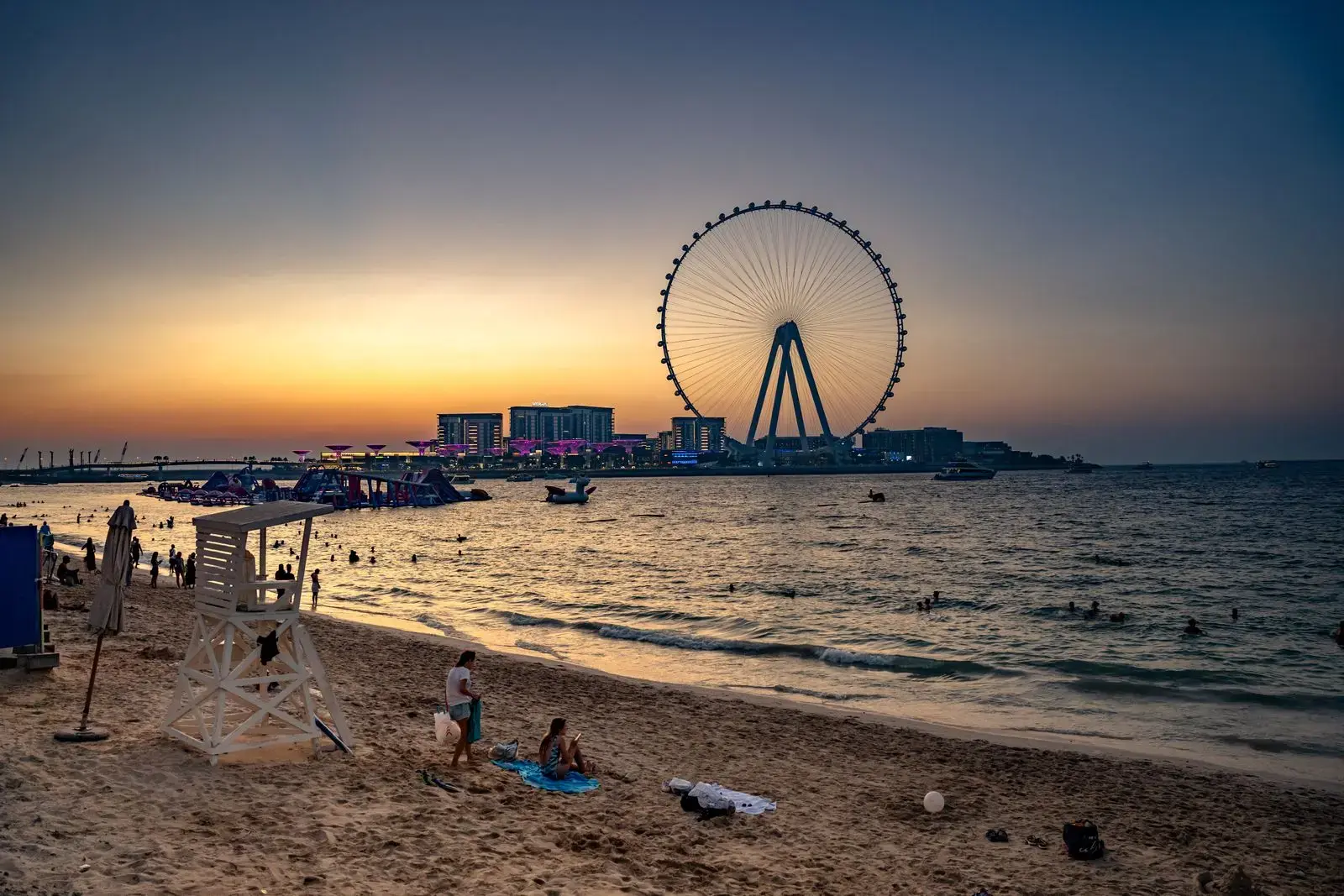 Photo by Selim Karadayı Serene sunset with Dubai Eye and beachgoers enjoying the evening by the water.