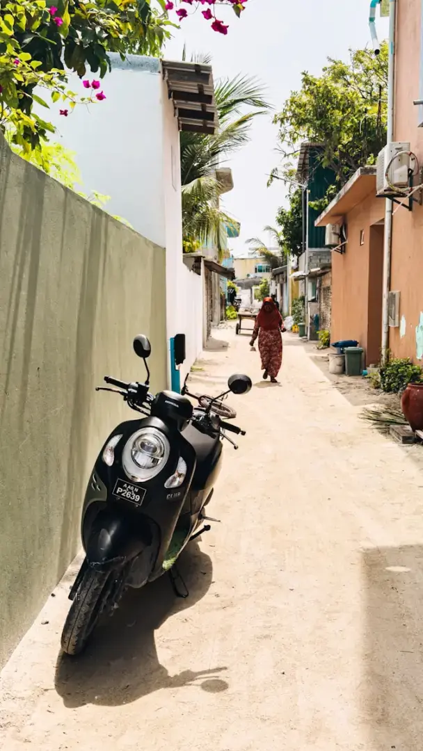 A person walks down a narrow street with a scooter