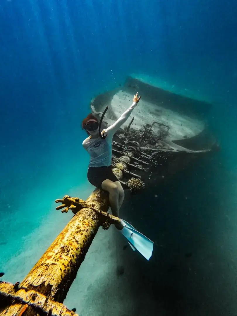 Person sits on shipwreck underwater with sun rays