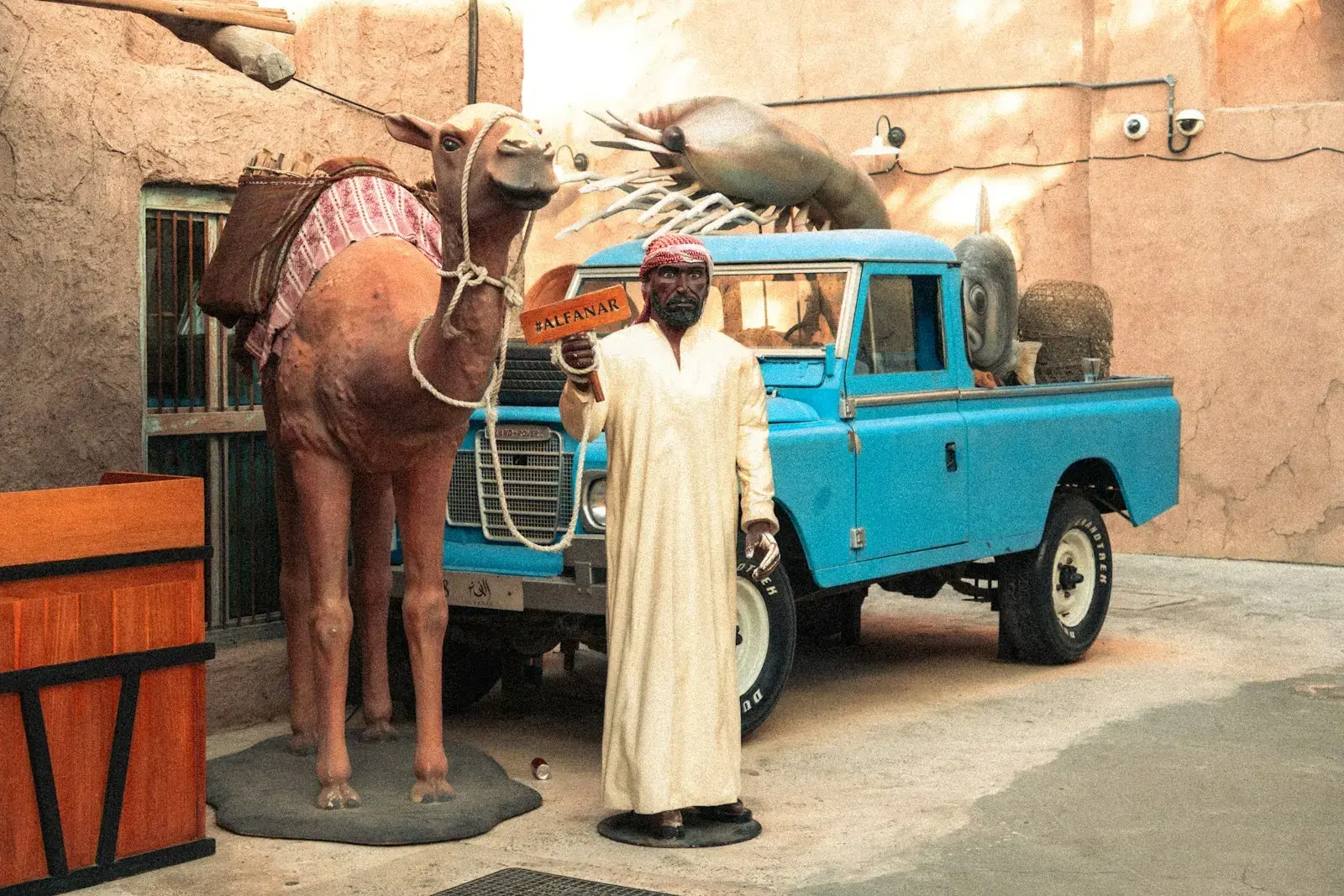 Man in traditional dress with camel and blue truck.