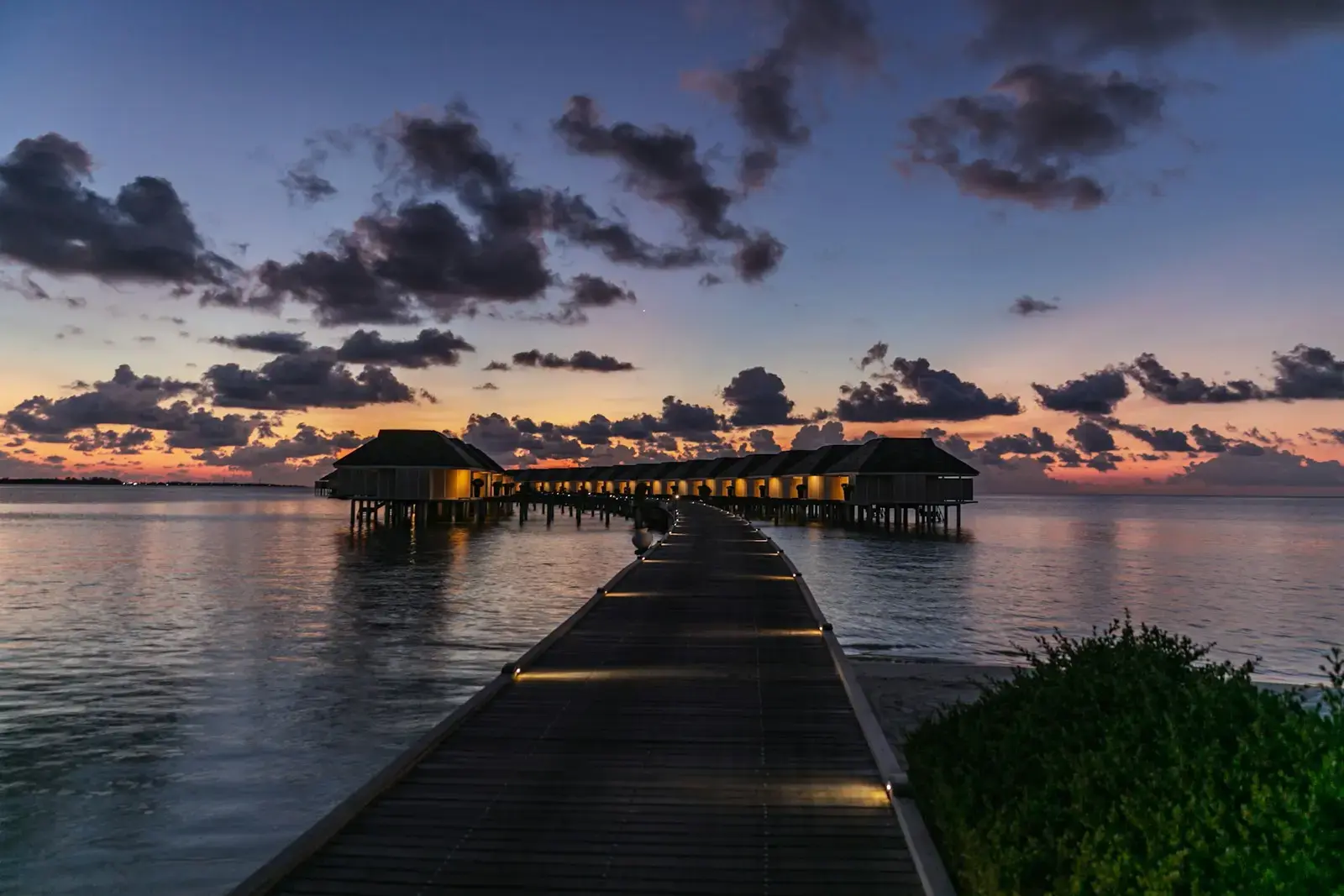 Wooden pier leading to overwater bungalows at sunset