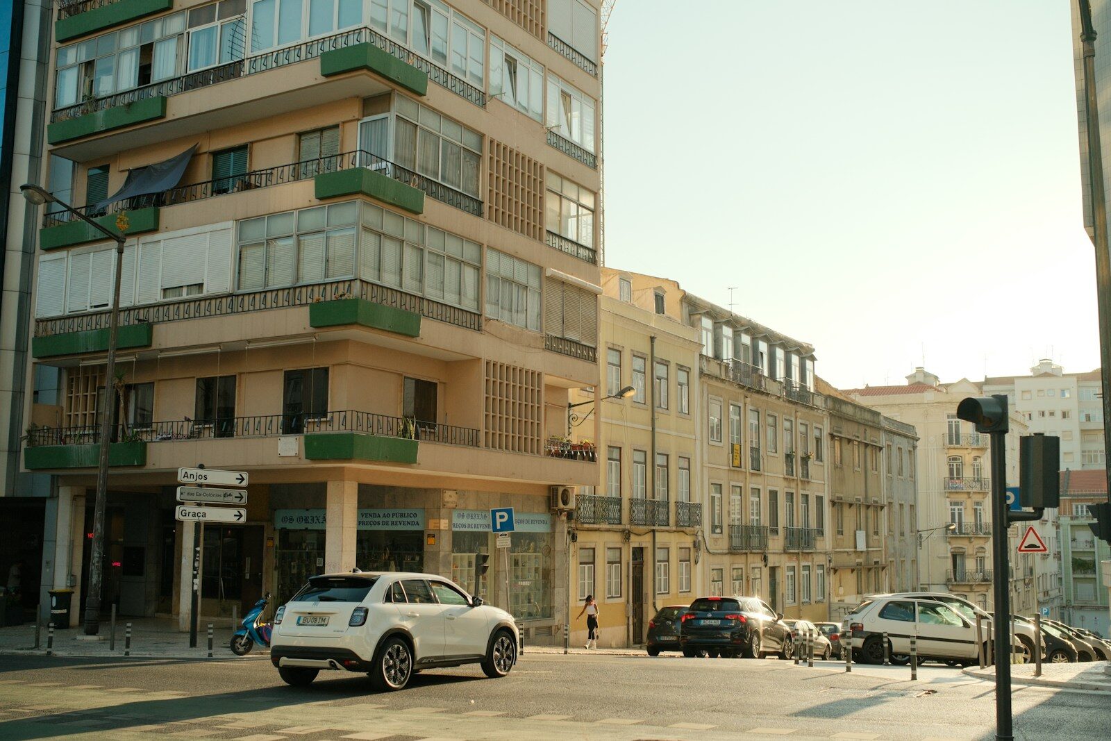 Photo by Timur Seyfelmlyukov A white car turning at a street corner in Lisbon with historic buildings